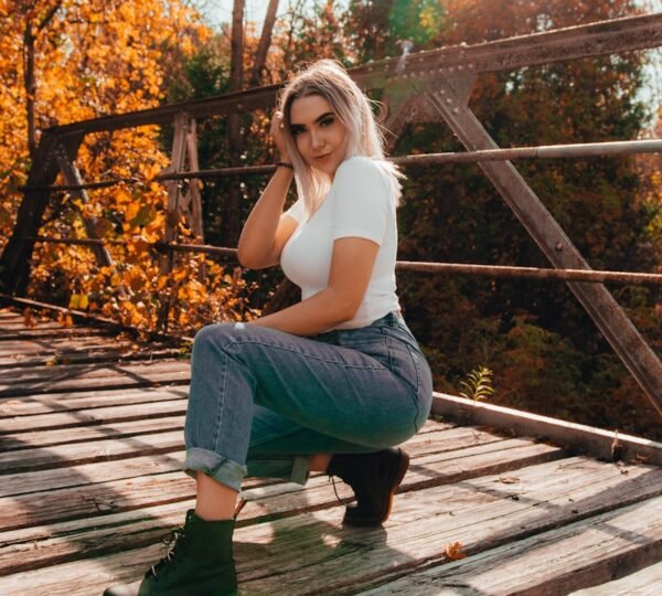 woman in white tank top and blue denim jeans sitting on brown wooden stairs